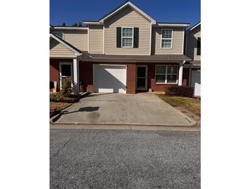 Two-story tan home with brick facade, and a concrete driveway leading to an attached garage at 233 Tara Commons Walk, Loganville, GA 30052