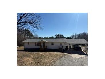 Ranch-style home with gray roof, carport, and mature trees, all under a bright blue sky at 1729 James Burgess Rd, Suwanee, GA 30024
