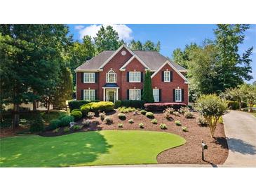 Charming two-story red brick home boasts manicured landscaping, lush greenery, and classic architectural details at 7215 Gresham Trce, Cumming, GA 30040