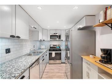 Modern kitchen featuring granite countertops, stainless steel appliances, white subway tile backsplash, and wood-look flooring at 6851 Roswell Rd # M12, Sandy Springs, GA 30328