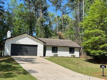 Charming single-story home featuring a dark garage door, well-manicured lawn, and beautiful surrounding trees at 1449 Albans Ct, Lithonia, GA 30058