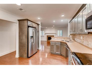Open kitchen view with stainless steel appliances, warm wood floors, and neutral stone tile backsplash at 2930 Torreya Se Way, Marietta, GA 30067