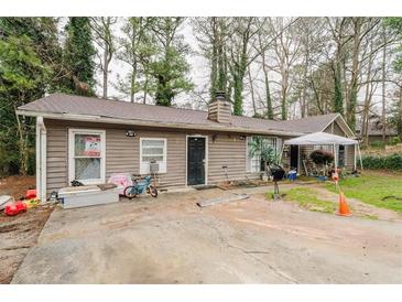 Tan single story home featuring a dark front door, brown roof and several deciduous trees surrounding it at 5461 Chuzzlewit Sw Ct, Lilburn, GA 30047