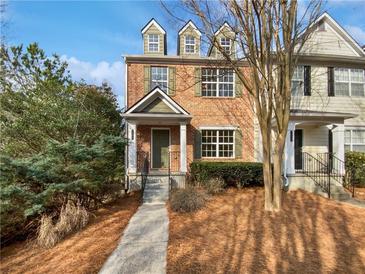 Charming brick townhome featuring dormer windows and landscaped front yard under a clear blue sky at 1100 Cotton Gin Dr, Woodstock, GA 30188