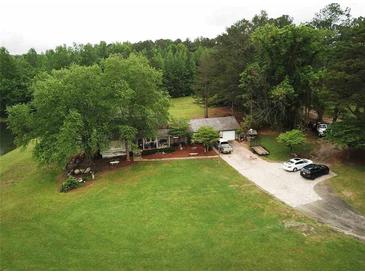 Quaint single-story home with lush front lawn and mature trees, offering serene lakeside living at 7275 Bishop Rd, Fairburn, GA 30213