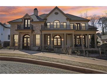 Elegant two-story home featuring a brick facade, wrought iron balconies, and a covered front porch at sunset at 440 Belada Blvd, Sandy Springs, GA 30342