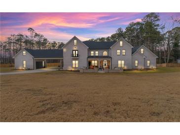 Stunning exterior showcasing a large white brick home with a portico, complemented by a spacious front yard and a colorful sunset at 2634 Greenes Ln, Powder Springs, GA 30127