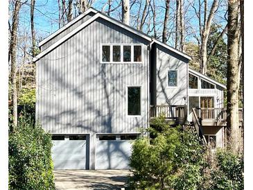 Two-story home featuring vertical siding, large windows, and an attached two-car garage, nestled amongst mature trees at 566 Hickory Hills Ct, Stone Mountain, GA 30083