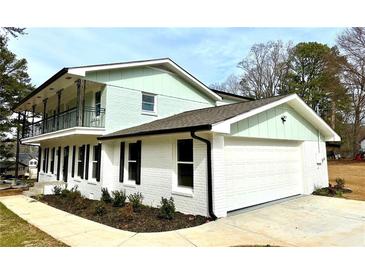 Two-story home features a white brick and light green exterior, black trim, a balcony and attached garage at 356 Greenwood Nw Dr, Lilburn, GA 30047