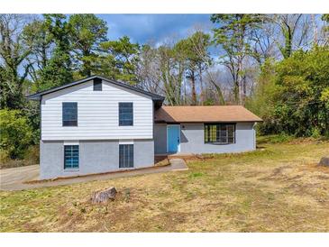 Charming split-level home with blue door and gray brick, nestled among mature trees and a yard at 6684 Heathrow Ln, Stone Mountain, GA 30087