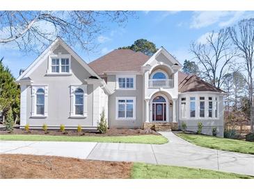 Elegant two-story home featuring a manicured lawn, arched windows, and a charming balcony at 7015 Polo Dr, Cumming, GA 30040