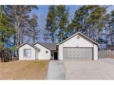 Charming one-story white home with a gray garage door surrounded by tall trees and a neatly maintained lawn at 975 Fox Valley Trl, Stone Mountain, GA 30088