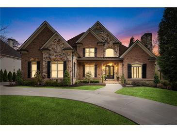 Beautiful brick and stone home with manicured lawn and inviting curb appeal at twilight at 8760 Colonial Pl, Duluth, GA 30097