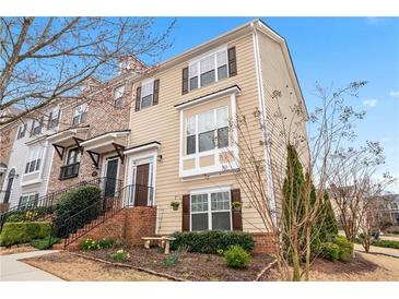 Charming two-story townhouse featuring light beige siding, dark shutters, a brick foundation and inviting front garden at 1262 Park Pass Row, Suwanee, GA 30024