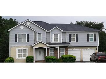 Two-story home featuring gray siding, black shutters, and a two-car garage, set against a lush green backdrop at 3551 Northgate Cv, Ellenwood, GA 30294