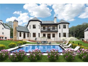 A luxurious pool area featuring a large pool, beautiful landscaping, and an elegant white brick home in the background at 10745 Shallowford Rd, Roswell, GA 30075