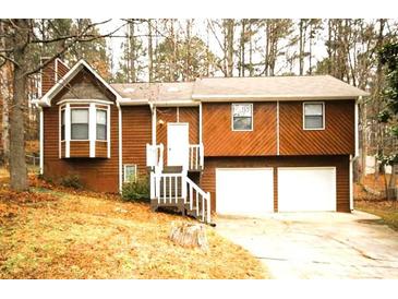 Charming home featuring a two-car garage, wood siding, and a manicured front lawn surrounded by mature trees at 5570 Deerfield Nw Pl, Kennesaw, GA 30144