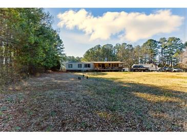 Spacious front yard featuring a mobile home with a covered porch, surrounded by trees at 1515 Ozora Rd, Loganville, GA 30052
