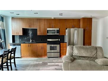 Open kitchen with wooden cabinets, stainless steel appliances, and black backsplash at 943 Peachtree Ne St # 704, Atlanta, GA 30309