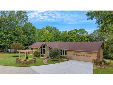 Charming single-story home with lush lawn, mature trees, and welcoming pergola over stone planter bed at 12040 Old Mountain Park Rd, Roswell, GA 30075
