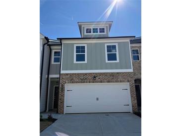 Two-story townhome with a two-car garage, brick facade, and sage green siding at 5615 Hislop Lane # 82, Mableton, GA 30126