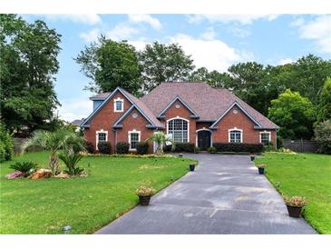 Beautiful brick home featuring a landscaped front yard, lush greenery, and a spacious driveway at 477 Glouchester Dr, Locust Grove, GA 30248