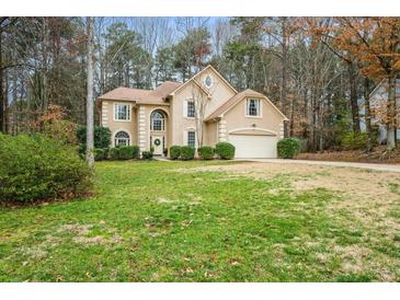 Charming tan two-story home featuring a manicured lawn and attached two car garage at 1605 Loblolly Ln, Cumming, GA 30041