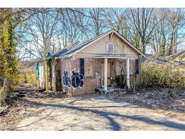 Overgrown lot with rundown brick house featuring boarded windows, graffiti, and weathered facade at 1340 North Avenue Ave, Atlanta, GA 30318