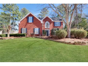 Charming two-story red brick home with manicured lawn, mature trees and complemented by lovely landscaping at 5569 Snowy Orchid Dr, Sugar Hill, GA 30518