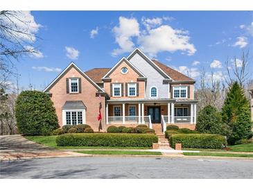 Beautiful brick home with covered front porch and manicured landscaping under a partly cloudy blue sky at 4865 Meadow Park Ln, Suwanee, GA 30024