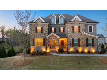 Charming stone-faced two-story home with manicured lawn and inviting entryway, illuminated by warm exterior lights at 4440 Croftshire Pl, Cumming, GA 30040