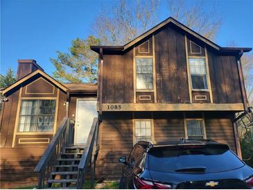Two-story home with brown wooden exterior, stairs leading to the front door, and a black car parked in front at 1085 Mainstreet Valley Dr, Stone Mountain, GA 30088