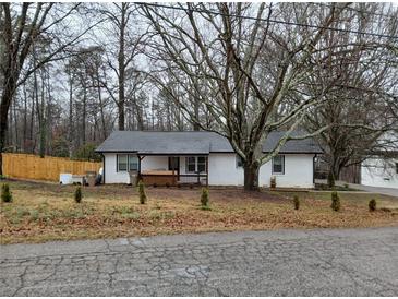 Charming single-story white brick home with black trim, a cozy front porch, and mature trees in the yard at 3250 Lee Dr, Buford, GA 30518