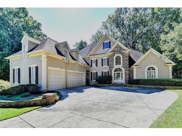Stately home with a large driveway, stone accents, and a three-car garage nestled among mature trees at 515 Butler National Dr, Johns Creek, GA 30097