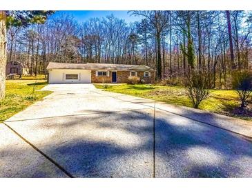 Ranch-style home with attached garage, large driveway, and front yard with mature trees at 8684 Chestnut Ln, Lithia Springs, GA 30122