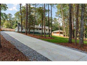 Long concrete driveway leading to a charming home nestled among mature trees and a tidy green lawn at 3345 Flowers Dr, Atlanta, GA 30337