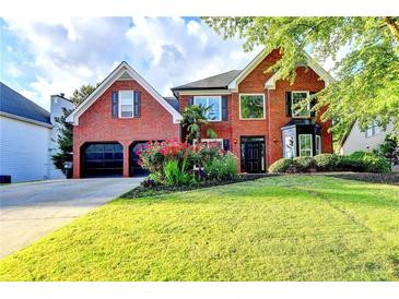 Stunning two-story red brick home with a well-manicured lawn, lush landscaping, and attached two-car garage at 1887 Lake Ridge Ter, Lawrenceville, GA 30043