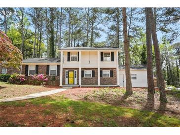 Well-maintained two-story home with a sidewalk leading to a yellow front door, surrounded by mature trees at 3973 Elmscourt Dr, Stone Mountain, GA 30083