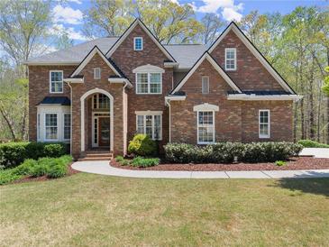 Stunning brick home boasts immaculate landscaping, arched entryway, and symmetrical design, nestled among mature trees at 6165 Lake Oak Lndg, Cumming, GA 30040