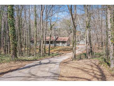 View of the home and detached garage down a long driveway lined with trees in a wooded lot at 30 Apache Ct, Locust Grove, GA 30248