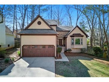 Charming home featuring a two-car garage, neutral stucco, brick accents, and mature trees around the perimeter at 216 Tennis Court Nw Ln, Kennesaw, GA 30144