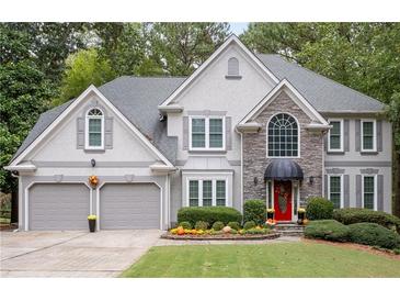 Charming two-story home features a manicured lawn, gray siding, stone accents, and a two-car garage at 3202 Eagle Watch Dr, Woodstock, GA 30189