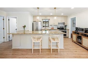 Bright kitchen featuring an island with a granite countertop, stainless steel appliances, and modern pendant lighting at 2466 Thrasher Rd, Buford, GA 30519