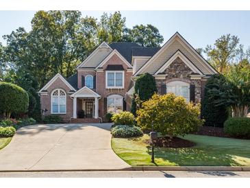 Beautiful two-story brick and stone home with lush landscaping and a long driveway leading to a spacious garage at 7085 Wakehurst Pl, Cumming, GA 30040