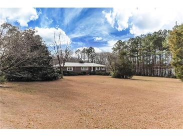 A ranch-style brick home with a well-manicured lawn and mature trees against a beautiful blue sky at 2443 Highway 92 S, Fayetteville, GA 30215