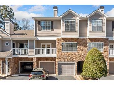 Attractive townhouse exterior with stone accents, covered parking, and balcony on a sunny day at 407 The Crossings Ln, Woodstock, GA 30189
