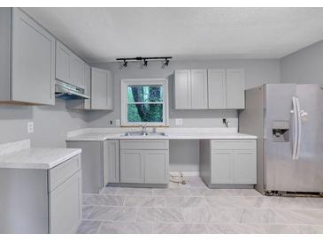Well-lit kitchen with stainless steel refrigerator, stylish grey cabinets, and gray tiled flooring at 1513 Spruce Ridge Way, Stone Mountain, GA 30083