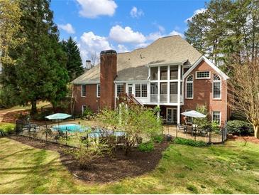 View of home's backyard with in-ground pool, brick exterior, large deck, and mature trees at 1544 Blue Bird Way, Cumming, GA 30041