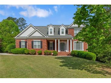 Traditional brick home featuring a welcoming front porch with white columns and a beautifully manicured lawn at 711 Wilhaven Ct, Loganville, GA 30052
