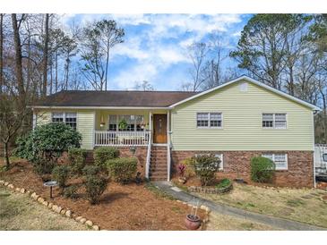 Charming yellow home featuring a cozy front porch, brick accents, and professionally landscaped yard with mature trees at 532 Rivercrest Dr, Woodstock, GA 30188
